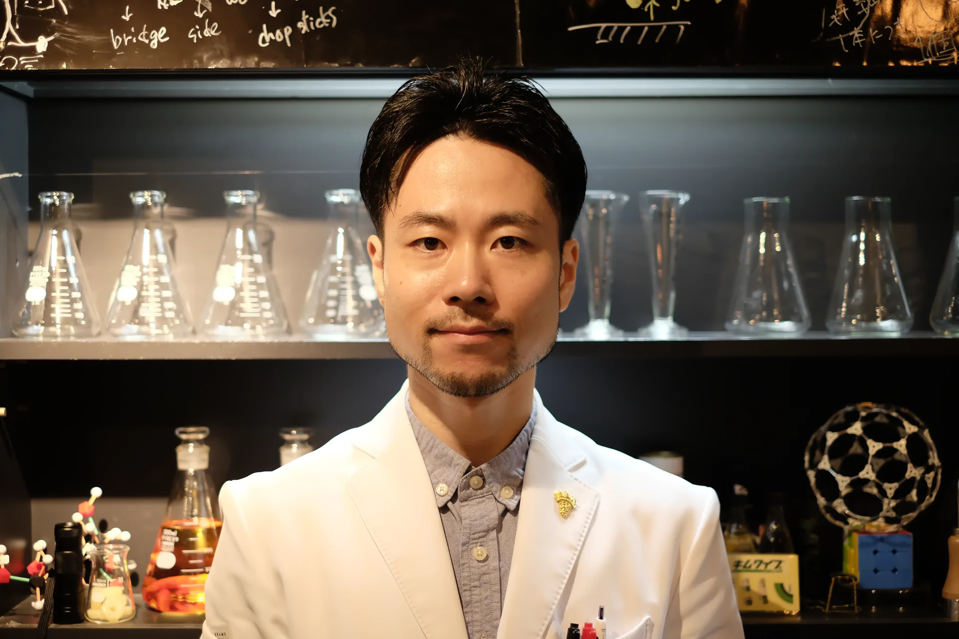 店内の実験器具を背景に白衣を着たScienceBar INCUBATORの店主
